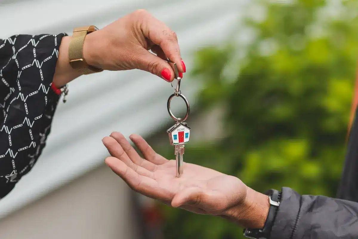 Une main tend une clé à porte-clés en forme de maison vers une autre main ouverte